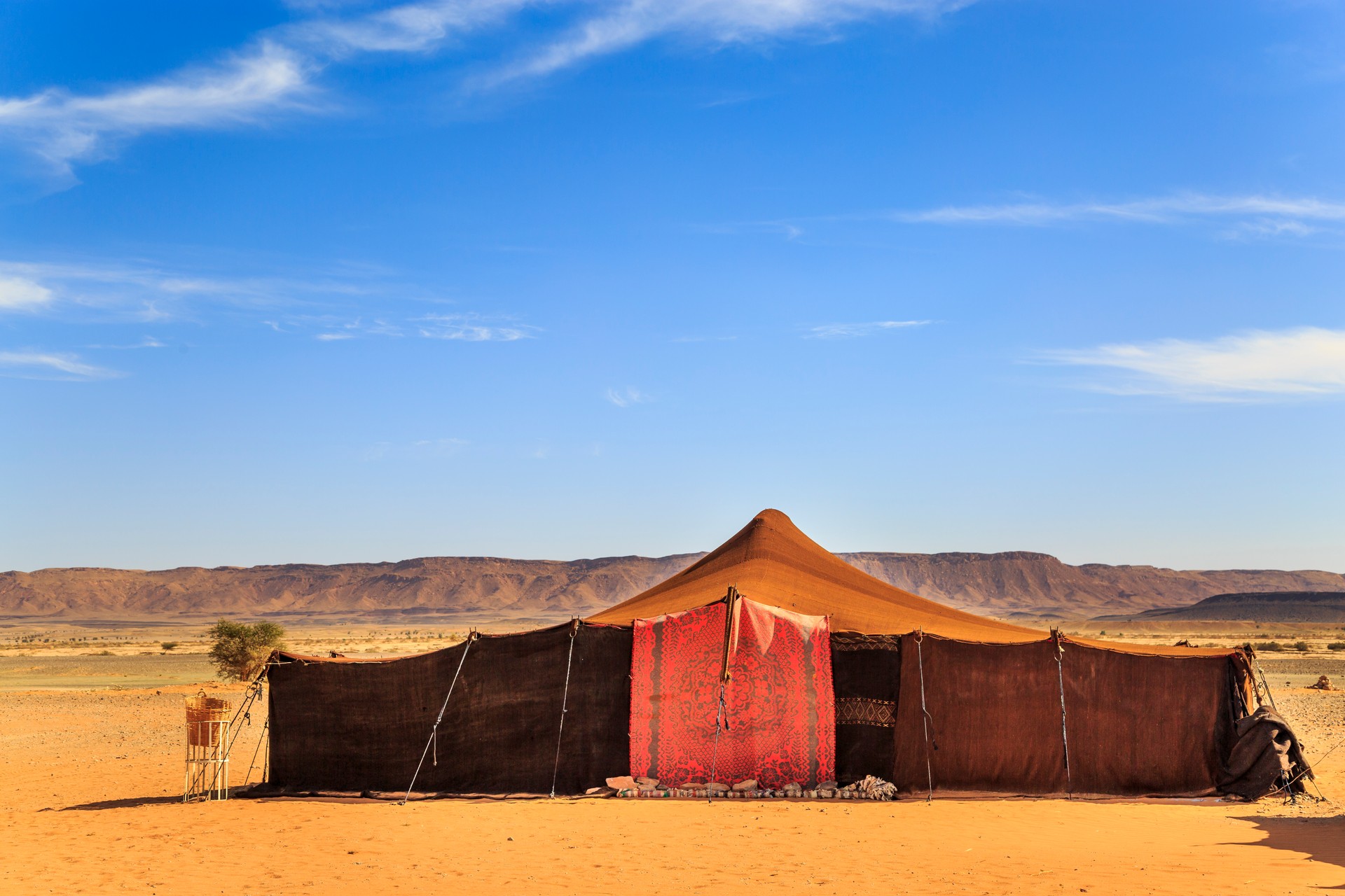 A tent made of camel skin in desert with mountains on background