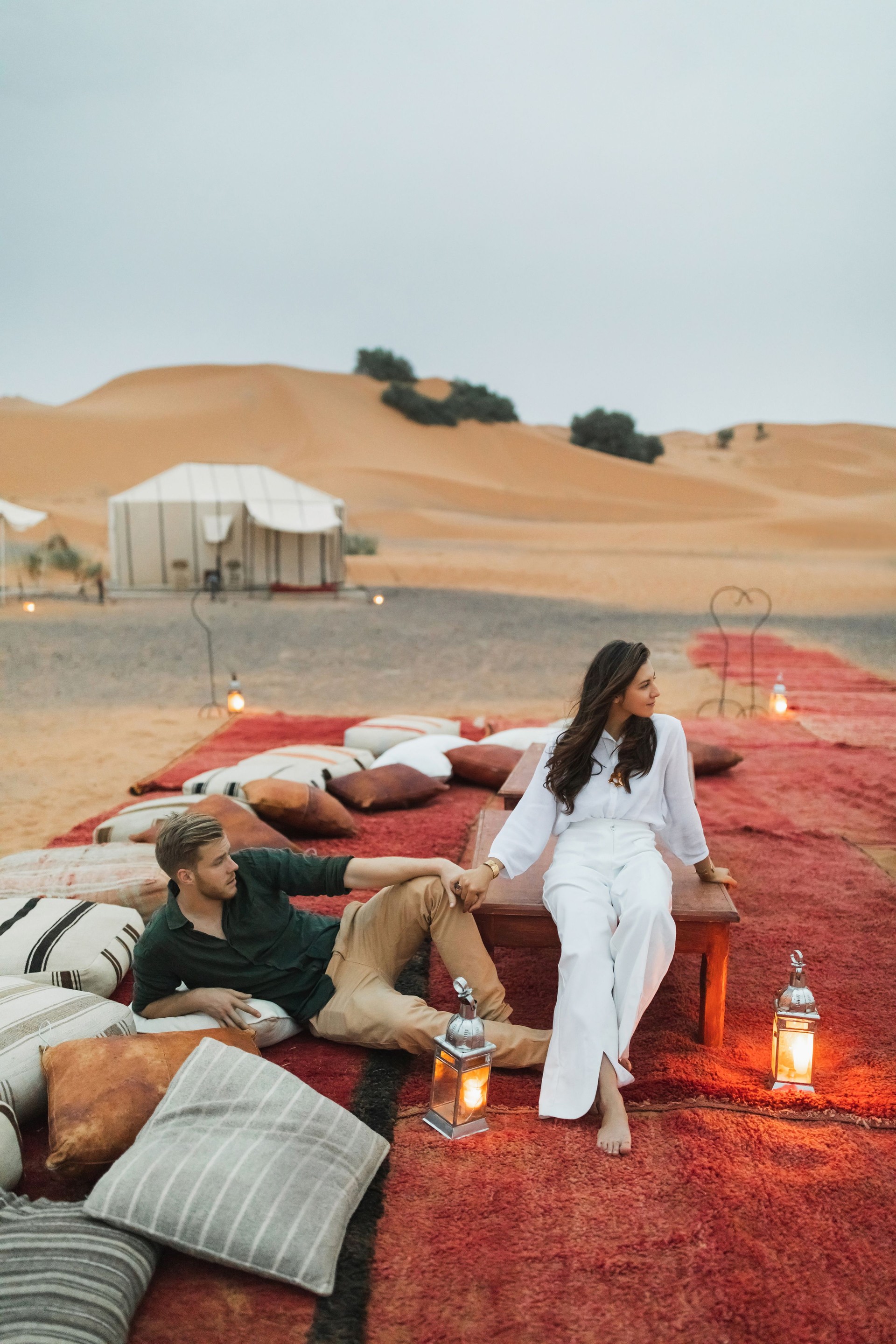 Stylish european couple in love enjoying evening together in luxury glamping camp in Sahara desert, Morocco. Romantic mood, lying on multicolor pillows.