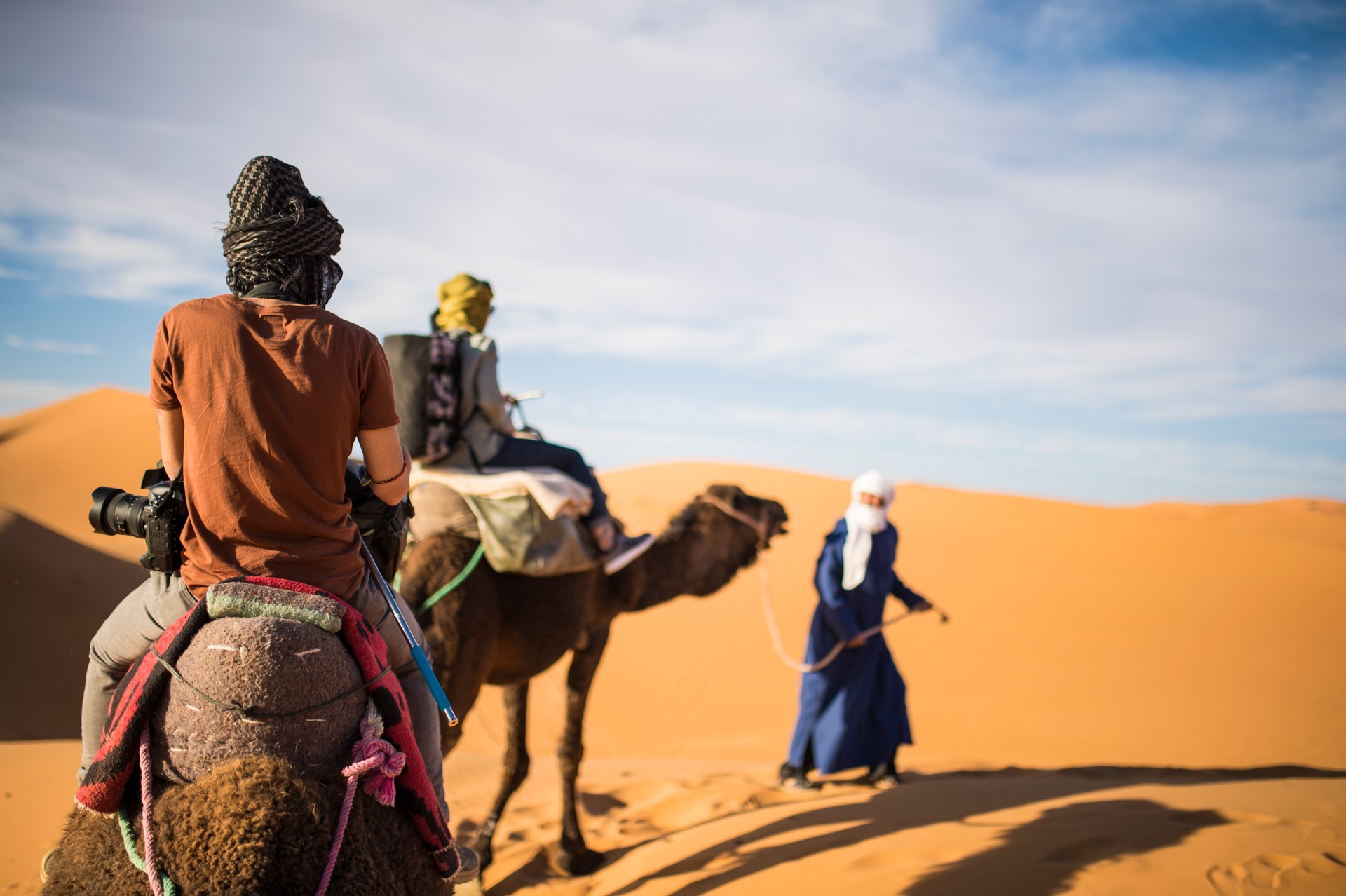 Tourists on camels going through the sand dunes in the Sahara Desert at sunset - Morocco.