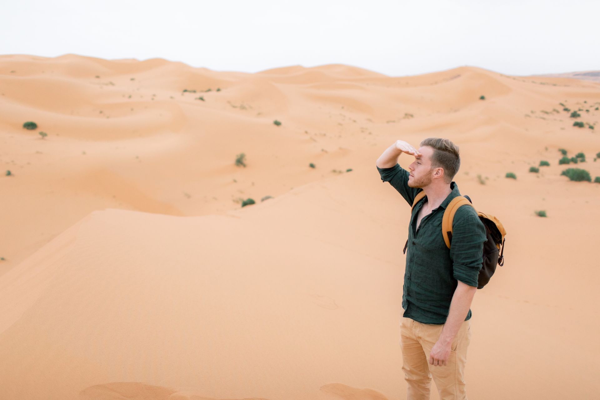 Handsome man traveller with backpack looking for yellow dunes in Sahara desert. Wanderlust travel concept. Space for text.